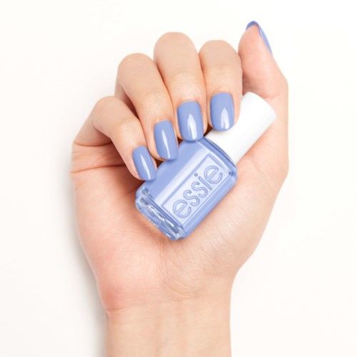 En hand med blåmålade naglar håller en liten flaska nagellack från Essie.