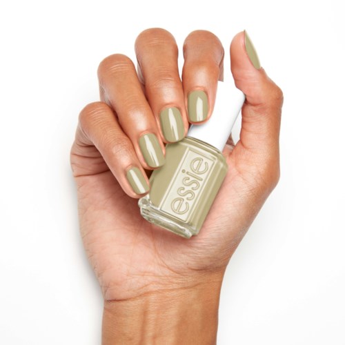 En hand med målade naglar håller en liten flaska med beige nagellack.