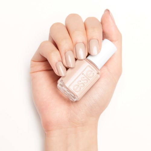 En hand med välmålade ljusbeige naglar som håller en flaska genomskinlig nagellack.