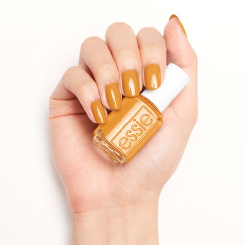 En hand med orange nagellack som håller en nagellacksflaska märkt 'essie' mot en vit bakgrund.