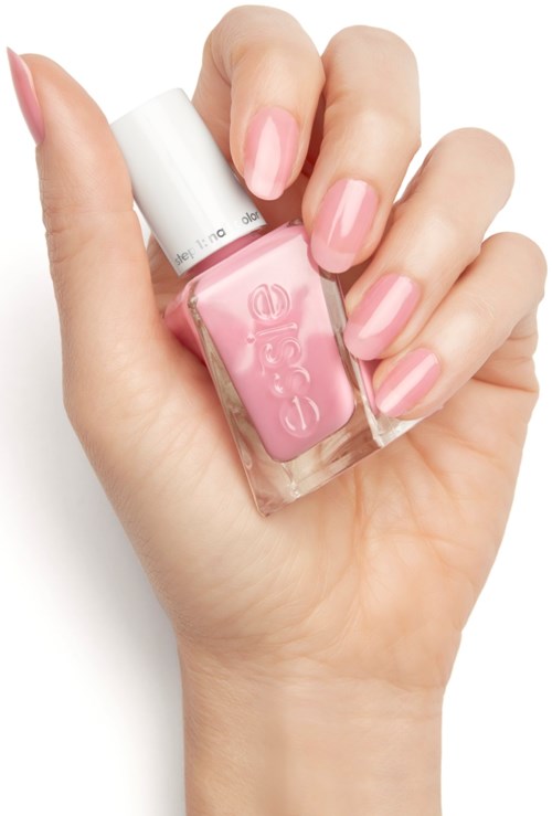 A hand with neatly painted pink nails holds a small pink bottle of nail polish.