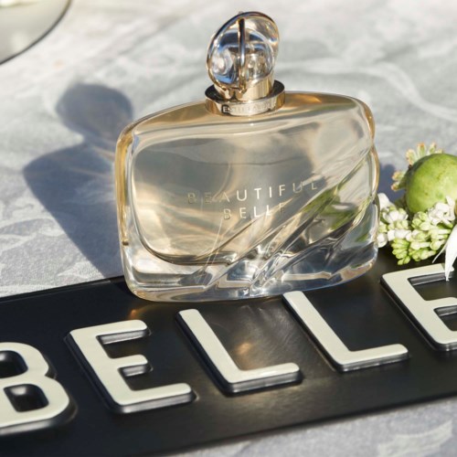 butelka perfum na powierzchni z kwiatami i słowem 'BELLE'.