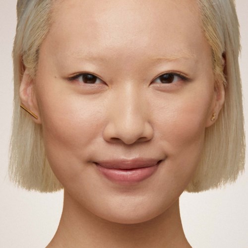 Eine Frau mit kurzen blonden Haaren, glatter Haut und einem freundlichen Lächeln. Sie trägt kleine Ohrringe und wirkt selbstbewusst.