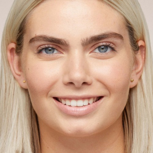 Kobieta z długimi blond włosami, jasną skórą, niebieskimi oczami i szerokim uśmiechem. Ma małe kolczyki i wygląda na szczęśliwą.