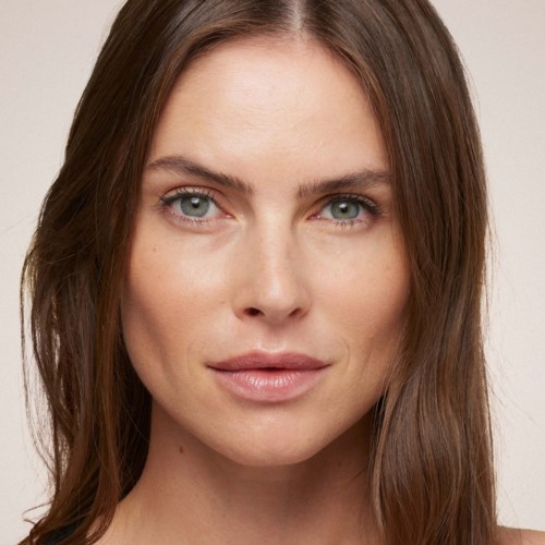 Eine Nahaufnahme einer Frau mit klarer Haut, blauen Augen, langem braunem Haar und einem sanften Lächeln.