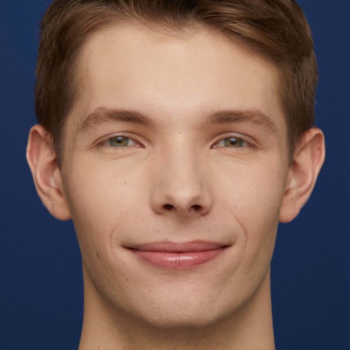 A young man with light skin and short brown hair smiling against a dark blue background.