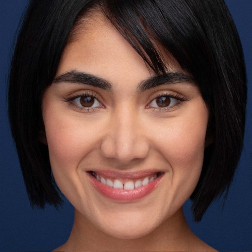 A young woman with short dark hair and brown eyes, smiling against a dark blue background.