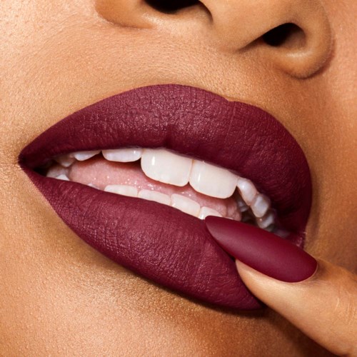 Close-up van lippen met donkere lipstick en een vinger die de lippen aanraakt.