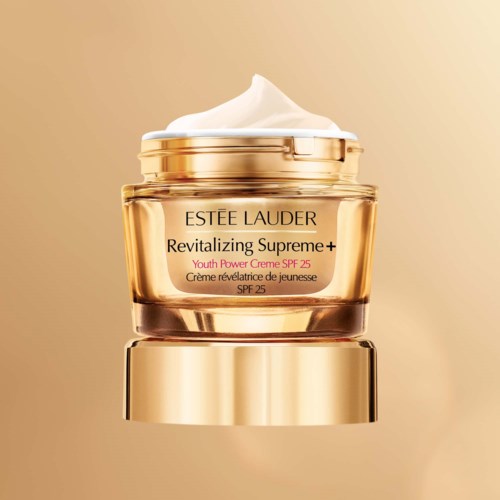 Ein goldener Behälter von Estée Lauder, gefüllt mit weißen Creme, auf einfachem Hintergrund.