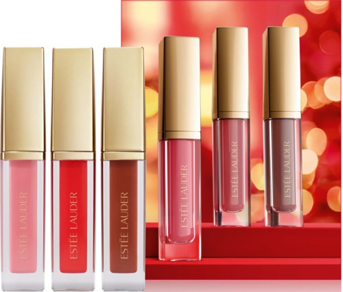 Zes lipglossen in roze en nude tinten op een display met een feestelijke rode achtergrond en onscherpe lichten.