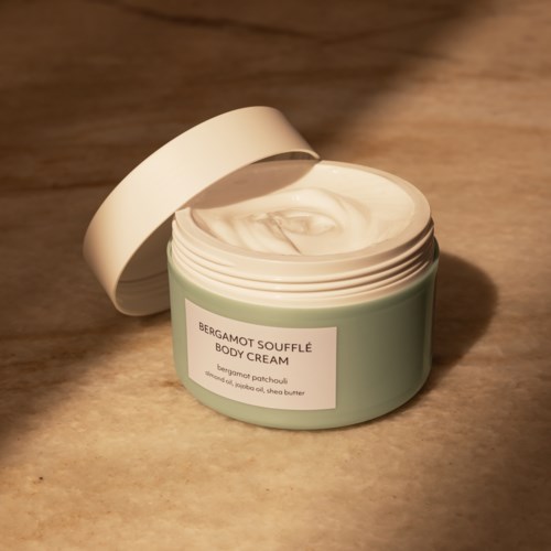 Bergamot Souffle -vartalovoide, jossa on avattu kansi, ja sisältä näkyy sileä voide.
