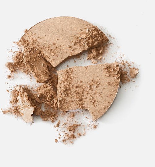Broken beige powder in a round shape with some pieces and crumbs scattered around.