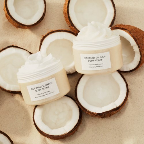 Two jars of coconut body cream and scrub are surrounded by halved coconuts.