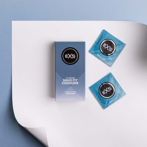 En æske med veganske snug fit-kondomer og to kondompakker på en hvid og blå overflade.