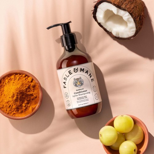 A brown soap bottle labeled Fabulous Conditioner surrounded by turmeric powder, green apples, and a halved coconut.