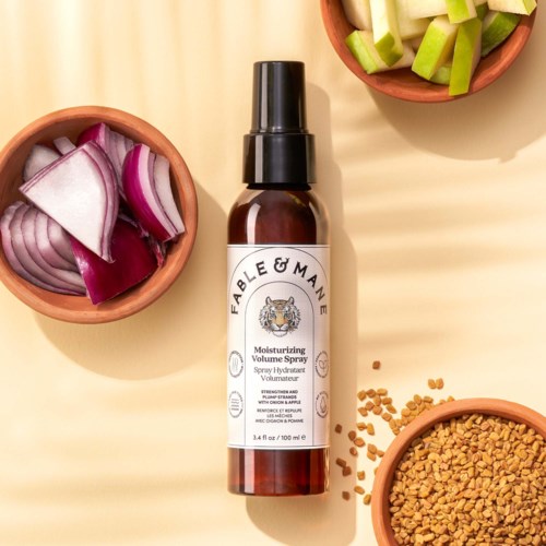 Moisturizing volume spray in a brown bottle with a black spray cap, surrounded by chopped red onions, green celery, and fenugreek seeds.