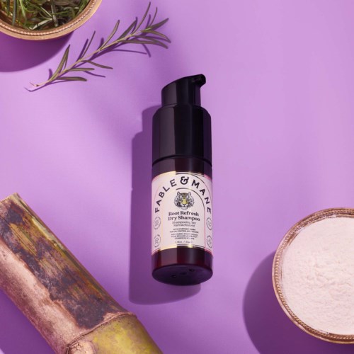 Bottle of roo refresh dry shampoo on a purple background with a plant and a bowl of powder nearby.