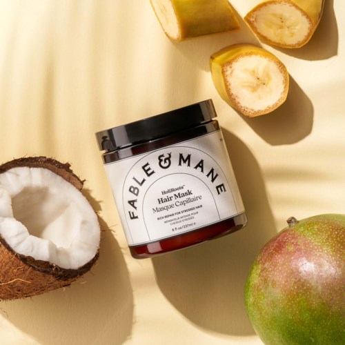 Hair mask jar with coconut, banana, and mango pieces around on a yellow background.