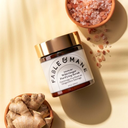 A jar of Fable & Mane Wild Ginger Purifying Scrub with ginger root and pink Himalayan salt around it.