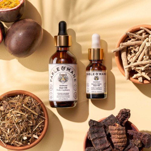 Two bottles of Fable & Mane hair oil with droppers, surrounded by natural herbs and dried plants.