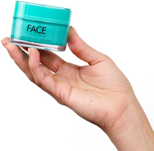 Eine Hand hält ein kleines türkisfarbenes Glas mit der Aufschrift 'FACE' und 'BOTANICAL CREAM'.