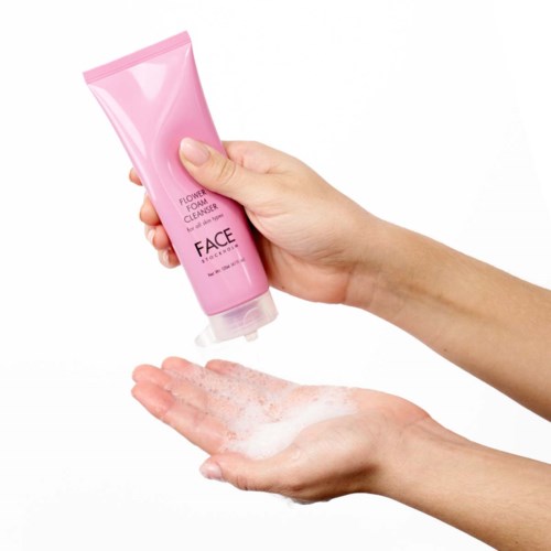 Eine Hand drückt rosa Gesichtsreiniger auf die offene Handfläche, mit Schaum bereit zur Reinigung.