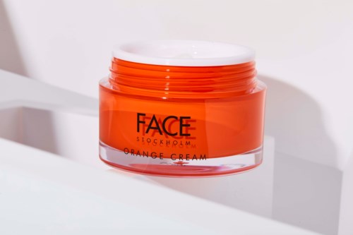 Ein Behälter mit orangecreme von FACE Stockholm auf weißer Oberfläche mit Schatten.