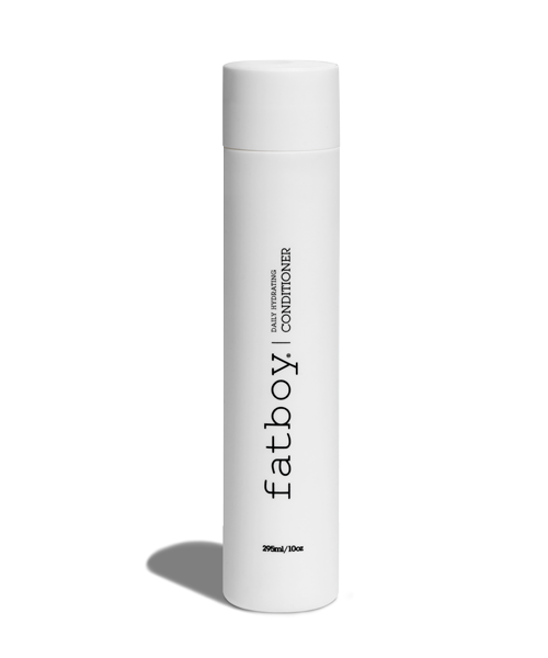 En vit cylindrisk flaska märkt 'fatboy! Conditioner' står upprätt på en vit yta.