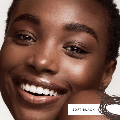 En leende kvinna med mörk hud, visar vita tänder, nära ansikte med naturlig makeup och texturerat hår.
