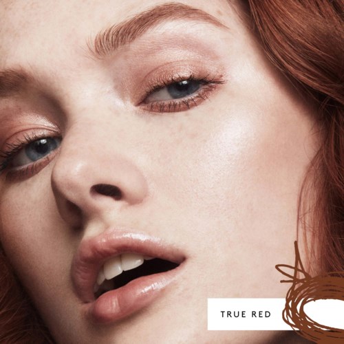 Närbild av en kvinna med rött hår, ljus hud och en subtil, naturlig makeup. Hon verkar luta sig eller titta lite.