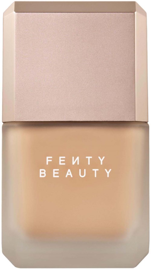 Foundationflaska från Fenty Beauty med rosaaktig lock och genomskinligt glas som visar den ljusbeiga vätskan inuti.