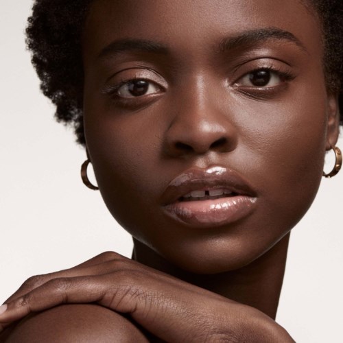 Close-up of a woman with dark skin, short curly hair, and wearing earrings, looking directly at the camera.