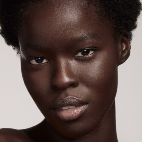 A young woman with short, natural curly hair and smooth, dark skin looks directly at the camera.