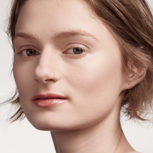 En ung kvinna med kort brunt hår, ljus hud och en näsring. Hon har ett neutralt uttryck och naturlig makeup.