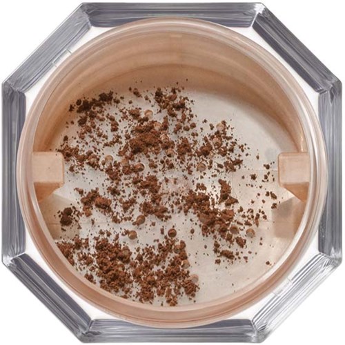 En burk innehåller beige pulver med bruna fläckar, sett uppifrån i en klar glaskärl.