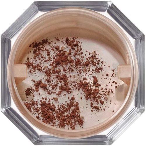 Ett runt behållare med beige kräm och brunt pulver på toppen, inuti ett oktagonalt glasställ.