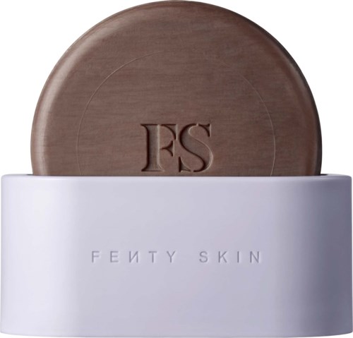 A brown round object with 'FS' on it, placed in a white container with 'FENTY SKIN' text.