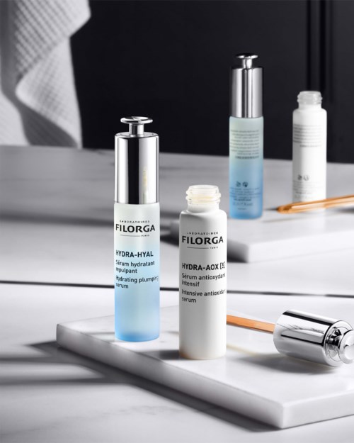 Skincare bottles and a roller on a white surface with a dark background.