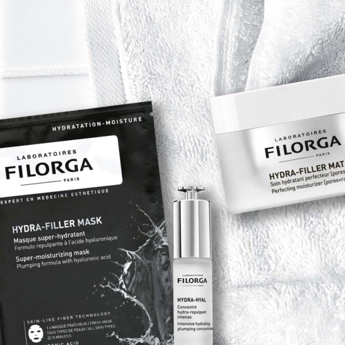Två hudvårdsprodukter, en svart och en vit, placerade på ett mjukt, vitt texturerat tyg. Den svarta förpackningen är märkt hydra-filler mask.