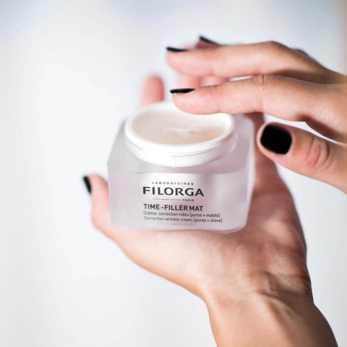 En hand håller ett krus med kräm märkt 'Filorga Time-Filler Mat' för hudavglättning och shinebekämpning.
