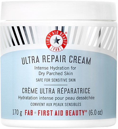 En vit burk med en etikett som visar produktnamn, fördelar, vikt och varumärke, First Aid Beauty, för torr hud.