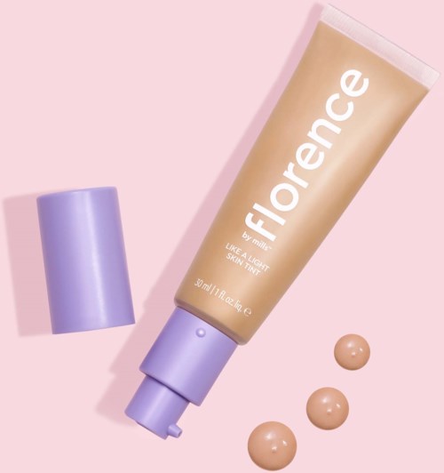 A beige tube of Florence skin tint with purple cap and three dollops of product on a pink background.