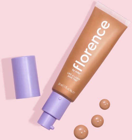 A tube of foundation with a purple cap and three dots of liquid on a pink background.