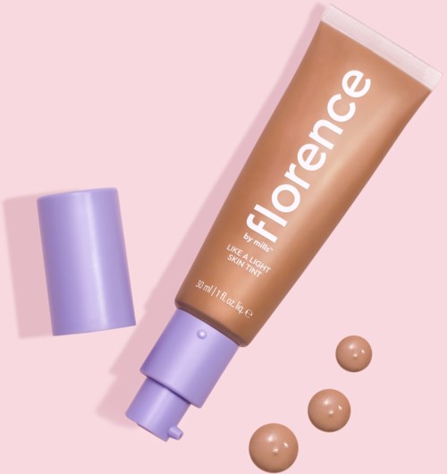 A tube of Florence skin tint with three small dots next to it, pink background, purple cap.