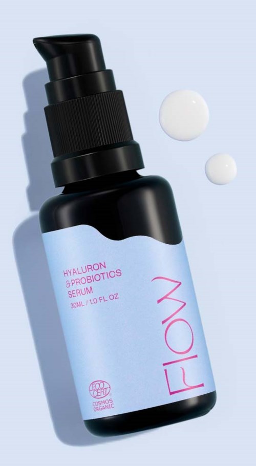 Musta pumppupullinen pullo, jossa lukee 'FLOW' ja 'Hyaluron & Probiotics Serum,' ja kaksi kreemipintaa lähellä.