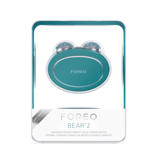 Ett turkost ansiktsapparat i ett paket med märket 'FOREO BEAR 2' för hudstramning och anti-chock. Den har två runda delar.