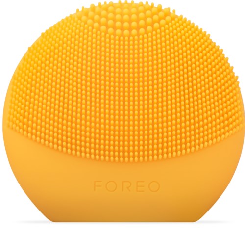 En gul, rund skönhetsenhet med mjuka borst på ytan, märkt "FOREO."