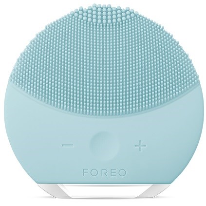 Een rond blauw apparaat met een getextureerd oppervlak bovenaan, plus- en minknopjes en het woord 'FOREO' onder.