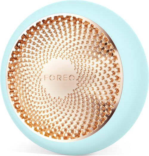En rund, ljusblå enhet med en guldaktig, texturerad yta och märket "FOREO" i mitten.