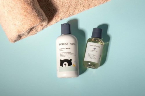 To Forest Kids-flasker, en med bjørne-design, plassert på en lys blå overflate med et brunt håndkle i nærheten.